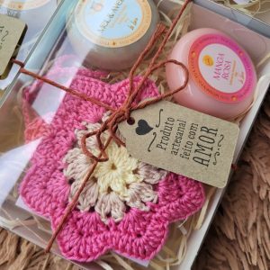 Kit presente com porta-sabonete em crochê rosa-choque em formato de flor e dois sabonetes artesanais La Luce (Mel & Aveia e Manga Rosa), em caixa transparente com laço.