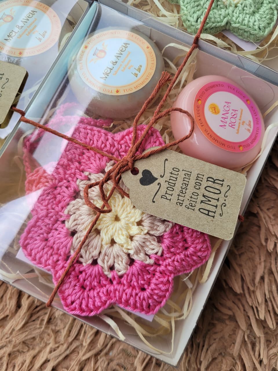 Kit presente com porta-sabonete em crochê rosa-choque em formato de flor e dois sabonetes artesanais La Luce (Mel & Aveia e Manga Rosa), em caixa transparente com laço.