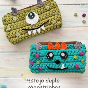 Dois estojos de crochê com carinha de monstrinho, um verde-oliva com um olho e chifres cinza, outro turquesa com dois olhos e chifres laranja.