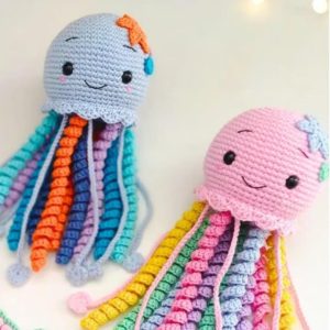 Dois polvinhos de crochê, um com cabeça cinza e tentáculos coloridos (laranja, azul, roxo), outro com cabeça rosa e tentáculos em tons pastel.