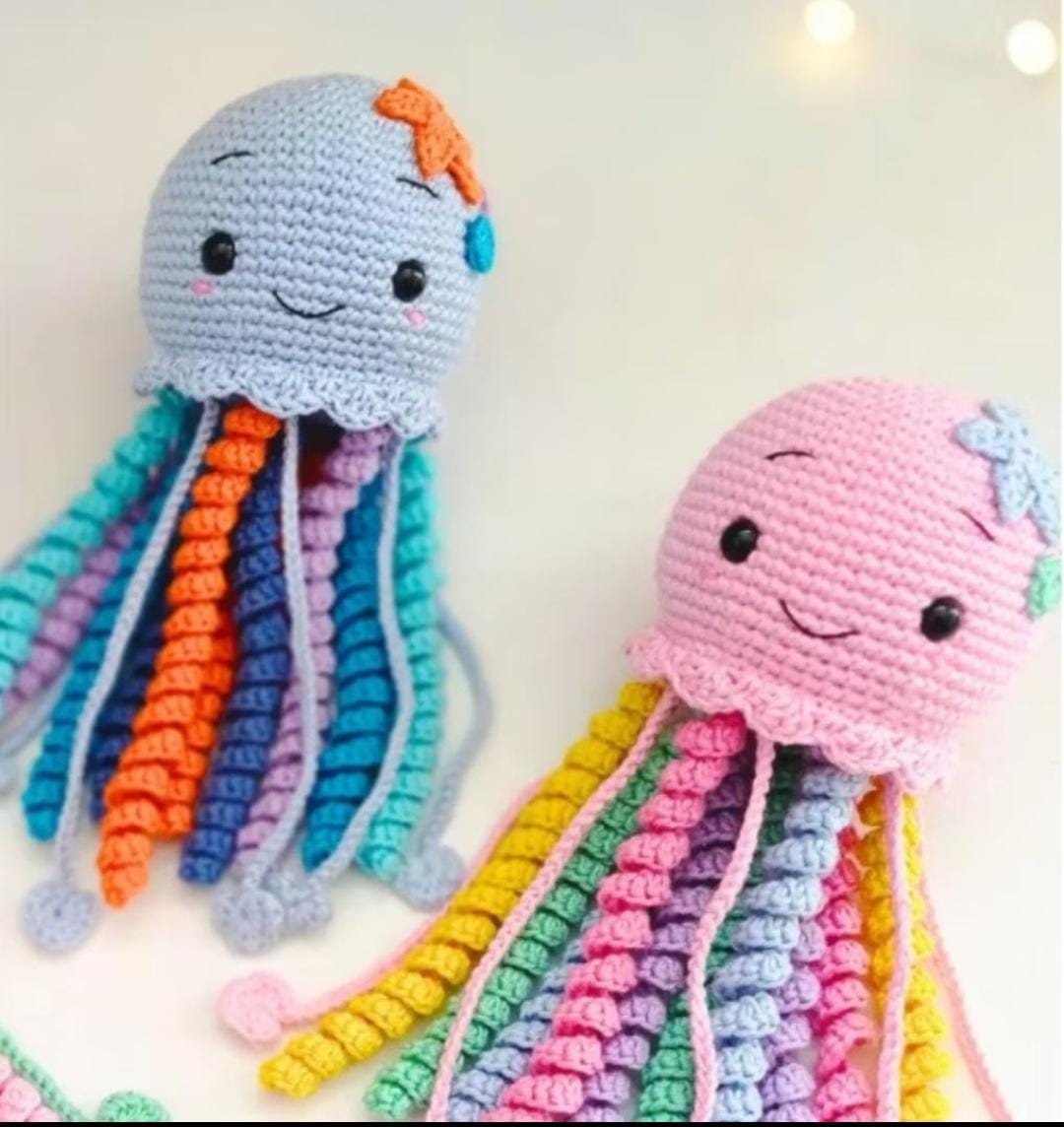 Dois polvinhos de crochê, um com cabeça cinza e tentáculos coloridos (laranja, azul, roxo), outro com cabeça rosa e tentáculos em tons pastel.