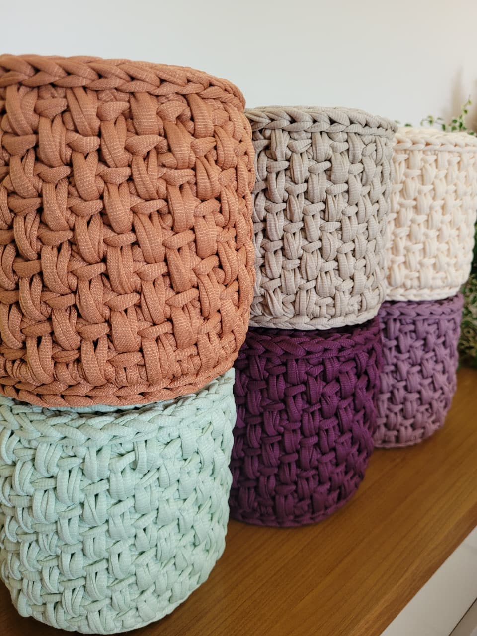 Seis capas de crochê para papel higiênico em cores diferentes (terracota, bege, cru, ameixa, rosé e verde-sálvia), empilhadas.