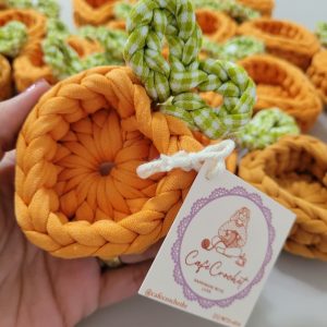 Porta-bombom de crochê em formato de cenoura laranja, com folhinhas em tecido xadrez verde e branco, tag Café Crochet ao lado.