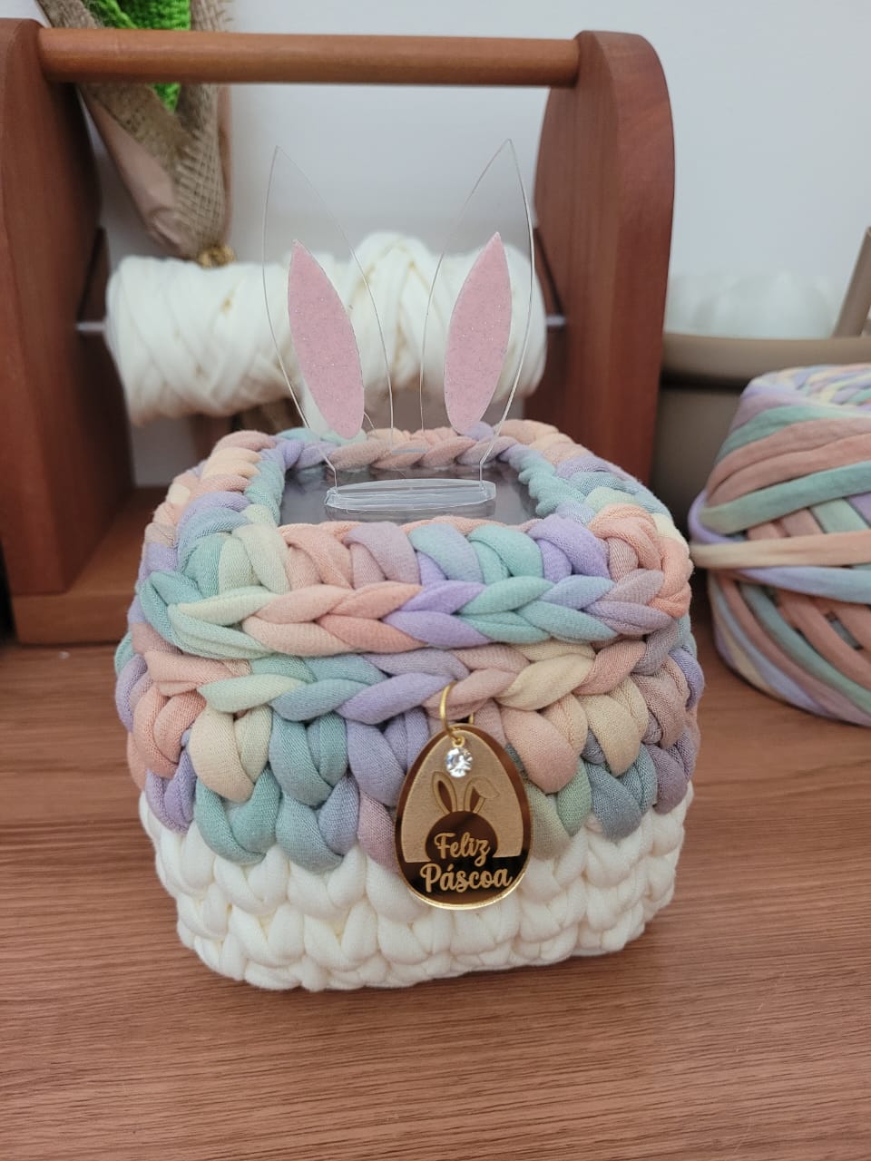 Cesto de crochê multicolor tons pastel, com orelhas de coelho em acrílico rosa e transparente, charm dourado Feliz Páscoa pendurado.