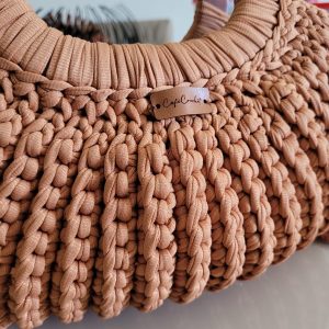 Bolsa de mão em crochê terracota, textura canelada densa, com alça de madeira redonda, tag Café Crochet visível.