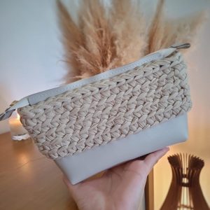 Nécessaire de crochê cru com base em courino claro e zíper, segurada na mão.