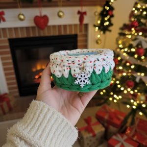 Potinho de crochê natalino com tampa em poá verde e branco, pingente de floco de neve, em frente a lareira decorada de Natal.