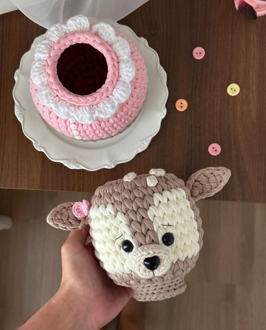 Cabeça de cervinho de crochê separada do corpo, revelando um potinho rosé e branco aberto, sobre prato de porcelana.